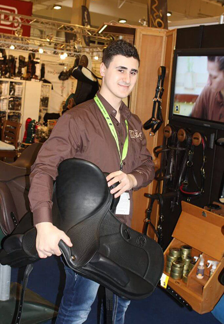 Auf dem Bild ist Herr Patric Hennig auf dem Hennig Messestand zu sehen. Unter dem Arm trägt er einen schwarzen Dressursattel und lacht.